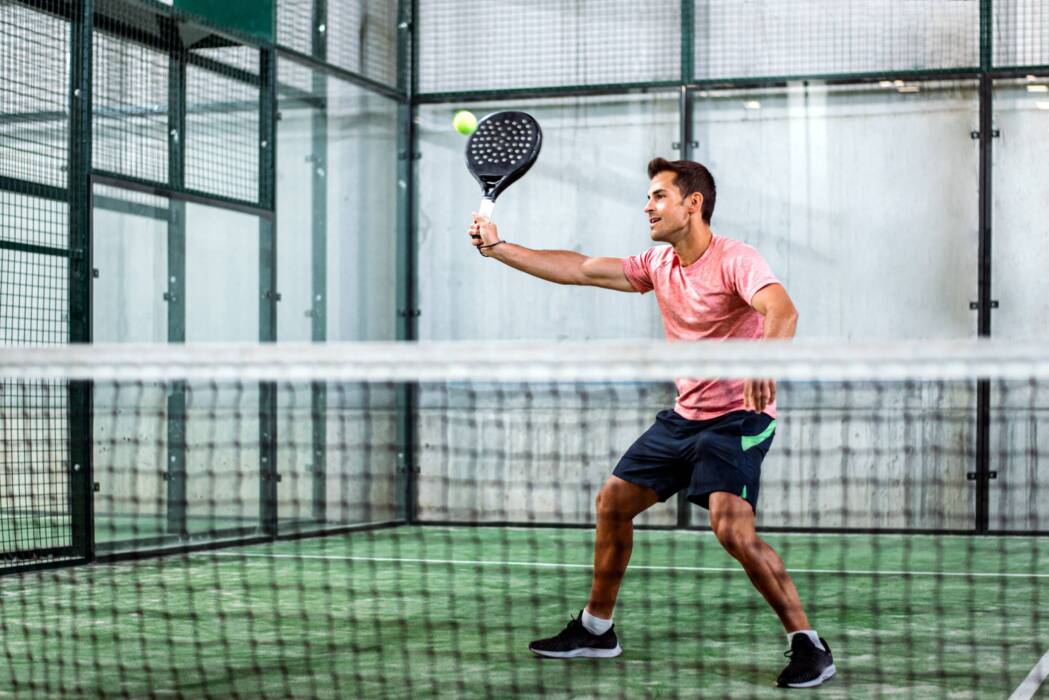 Man playing padel Man playing padel in a green grass padel court indoor behind the net